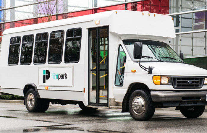 A clean and welcoming Impark HEALTH shuttle bus parked outside of a medical building.
